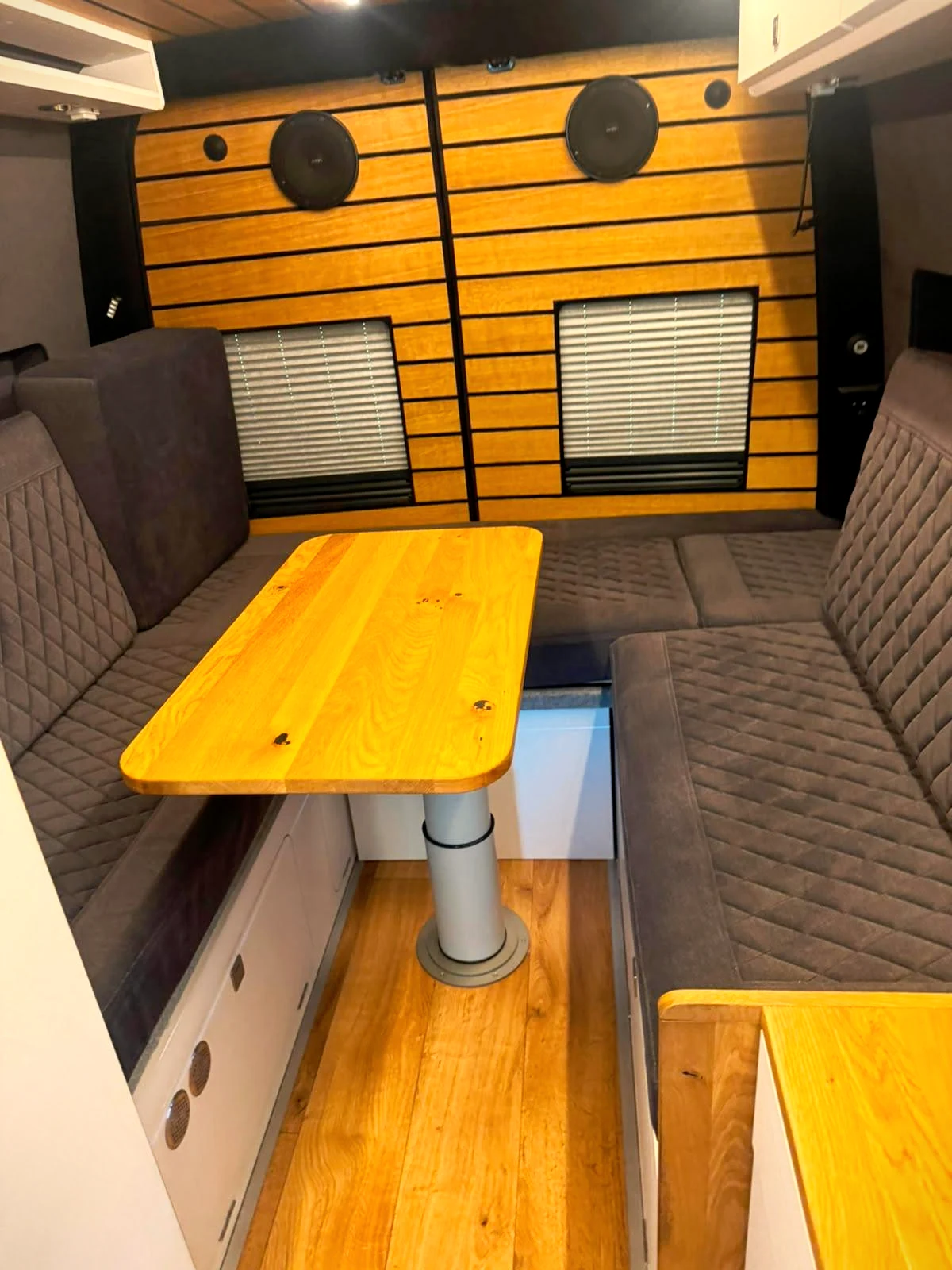Holzverkleidete Wand mit eingelassenen Lautsprechern und Massivholztisch im Busmacher Camper