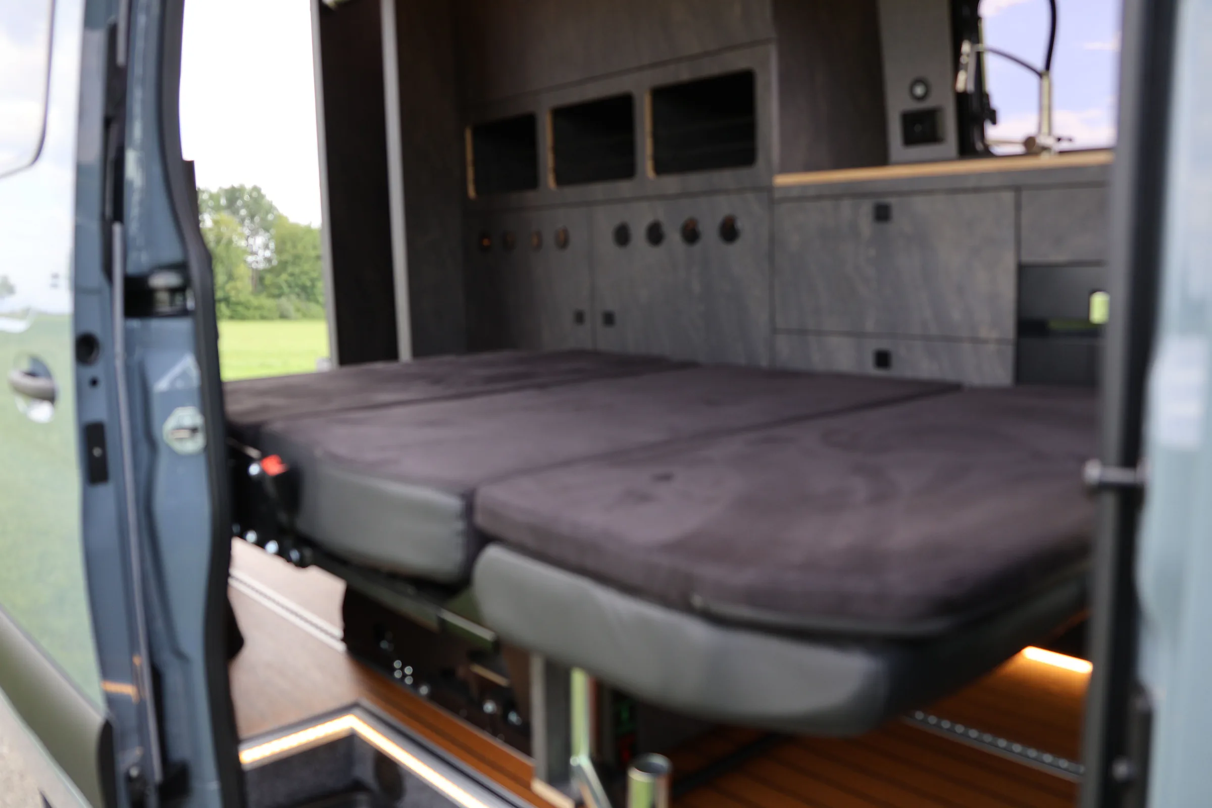 Zur Liegefläche umgebaute Sitzbank mit Polstern hinter der Schiebetür eines Busmacher Campers